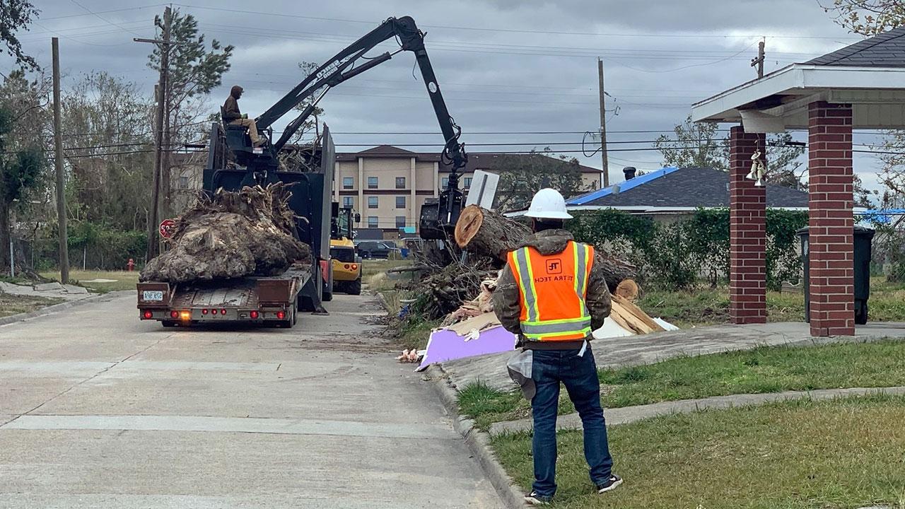 A Tetra Tech employee monitors a crane as it picks up disaster debris along a roadway on a cloudy day