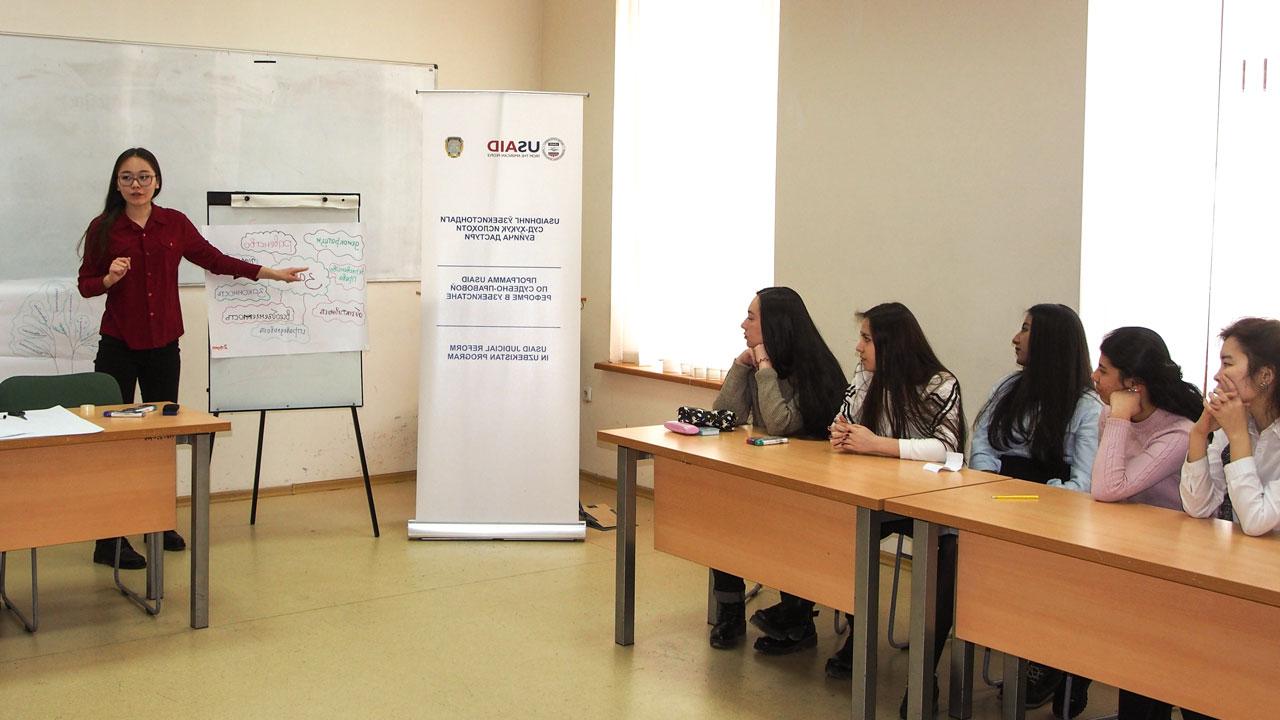 A lawyer, supported by the Tetra Tech-led Uzbekistan Justice and Rule of Law program, stands at the front of a meeting room presenting findings on a poster to a group of five people