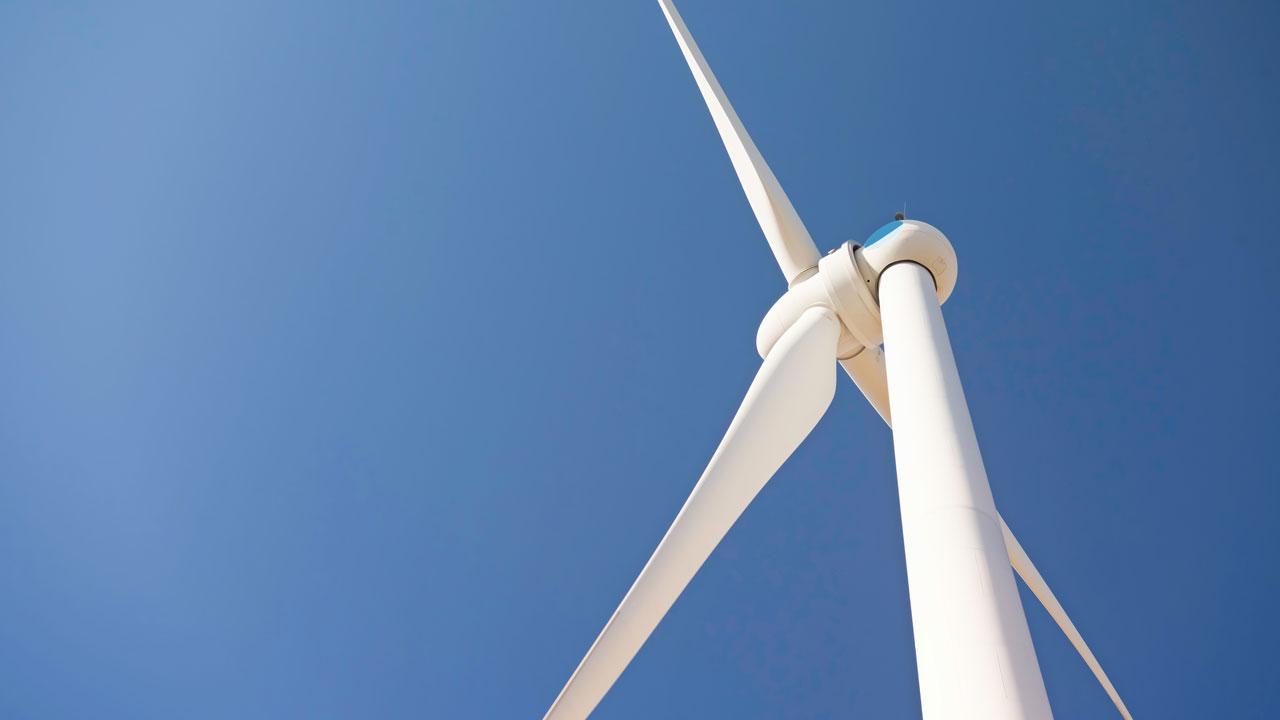 A wind turbine stands against a bright blue sky