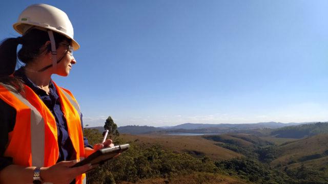 Worker wearing safety gear and holding a tablet looking towards a green landscape