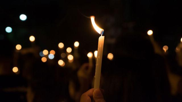 Hands holding lit candles at a night vigil