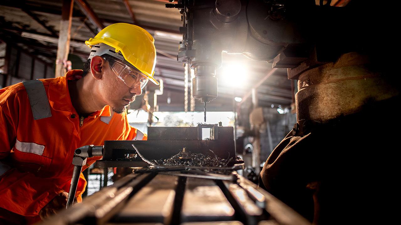 A person wearing orange work clothes and glasses stands beside the drilling rig and use metal drills in industrial