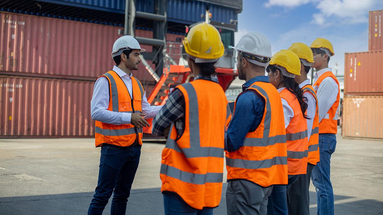 Four people wearing orange vests and hard hats gather for a meeting at a project site