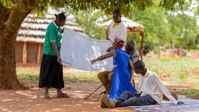 Community members, some sitting some standing, look over village demarcations in Uganda