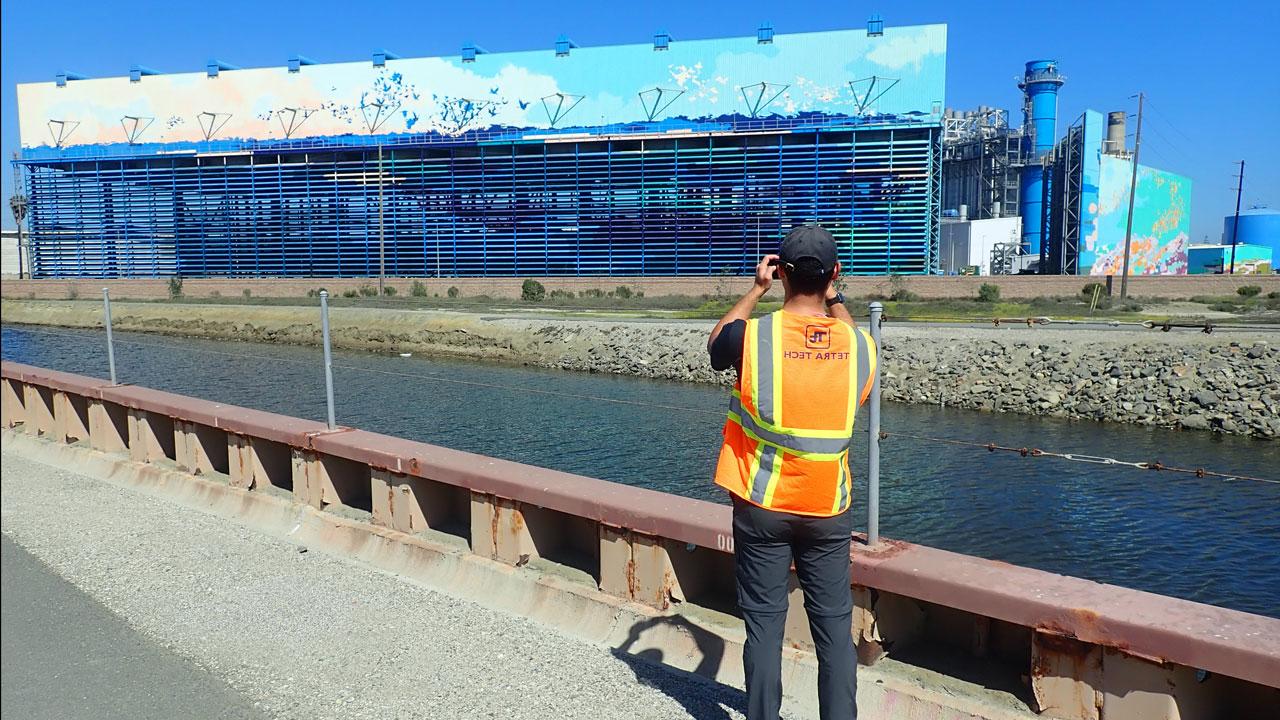 A Tetra Tech employee in a safety vest takes a photo of a water desalination plant during a channel inspection in California