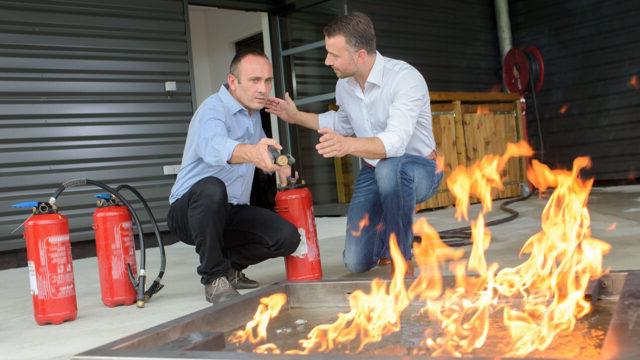 A trainer gives instructions to a student on how to extinguish a fire